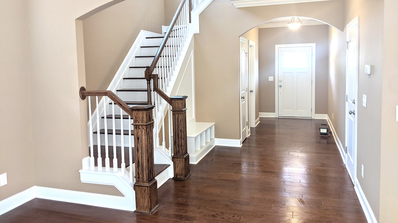 interior view of a home after it has been painted. This a brightly lit hallway with wood floors and a bannister.