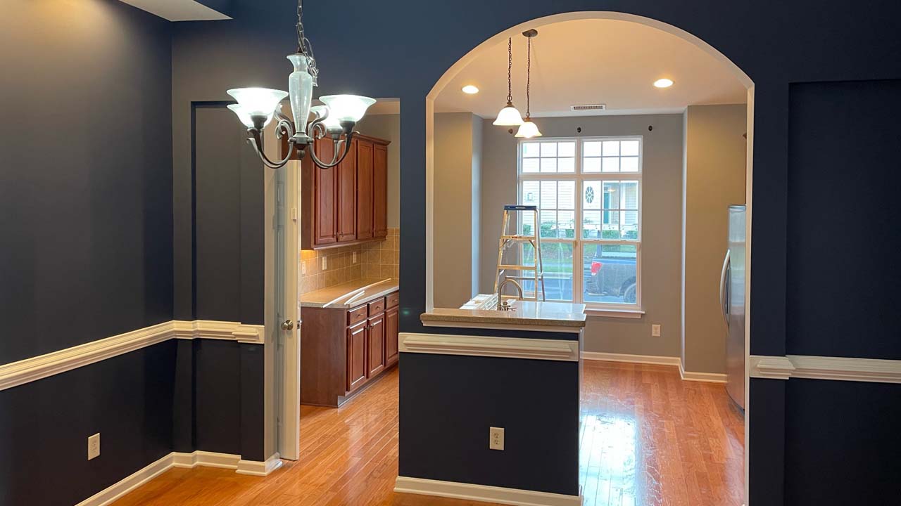 Image of the interior of a home that has been repainted. Navy blue walls, cherry red wood flooring. Well lit room. Sunny day outside.