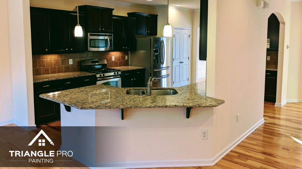 This is a kitchen painting project featuring dark cabinets and granite countertops by Triangle Pro Painting.