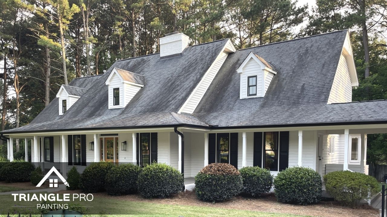 A freshly painted home exterior with white siding and black shutters by Triangle Pro Painting.