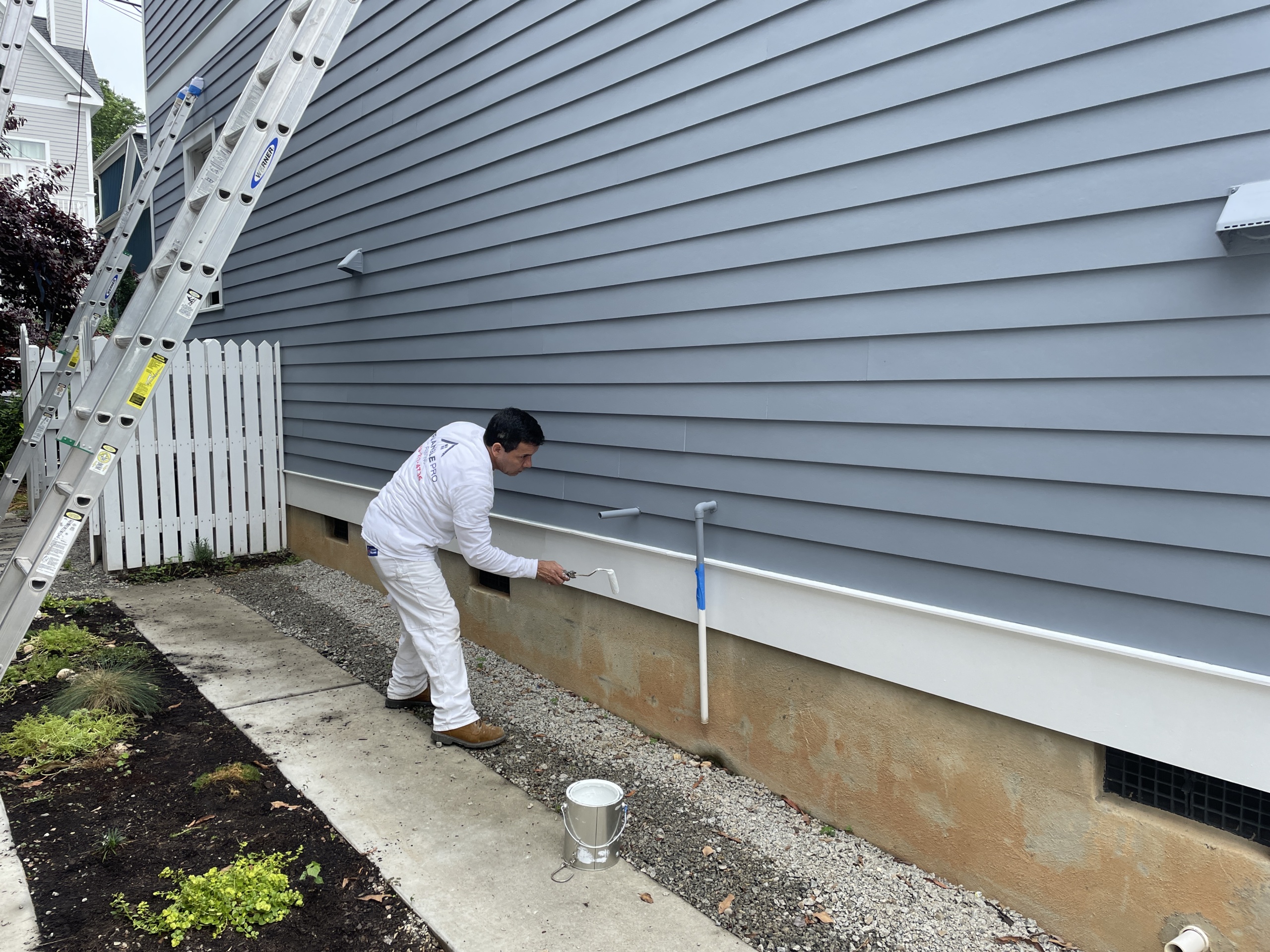 Professional exterior painter using sprayer on Raleigh home siding