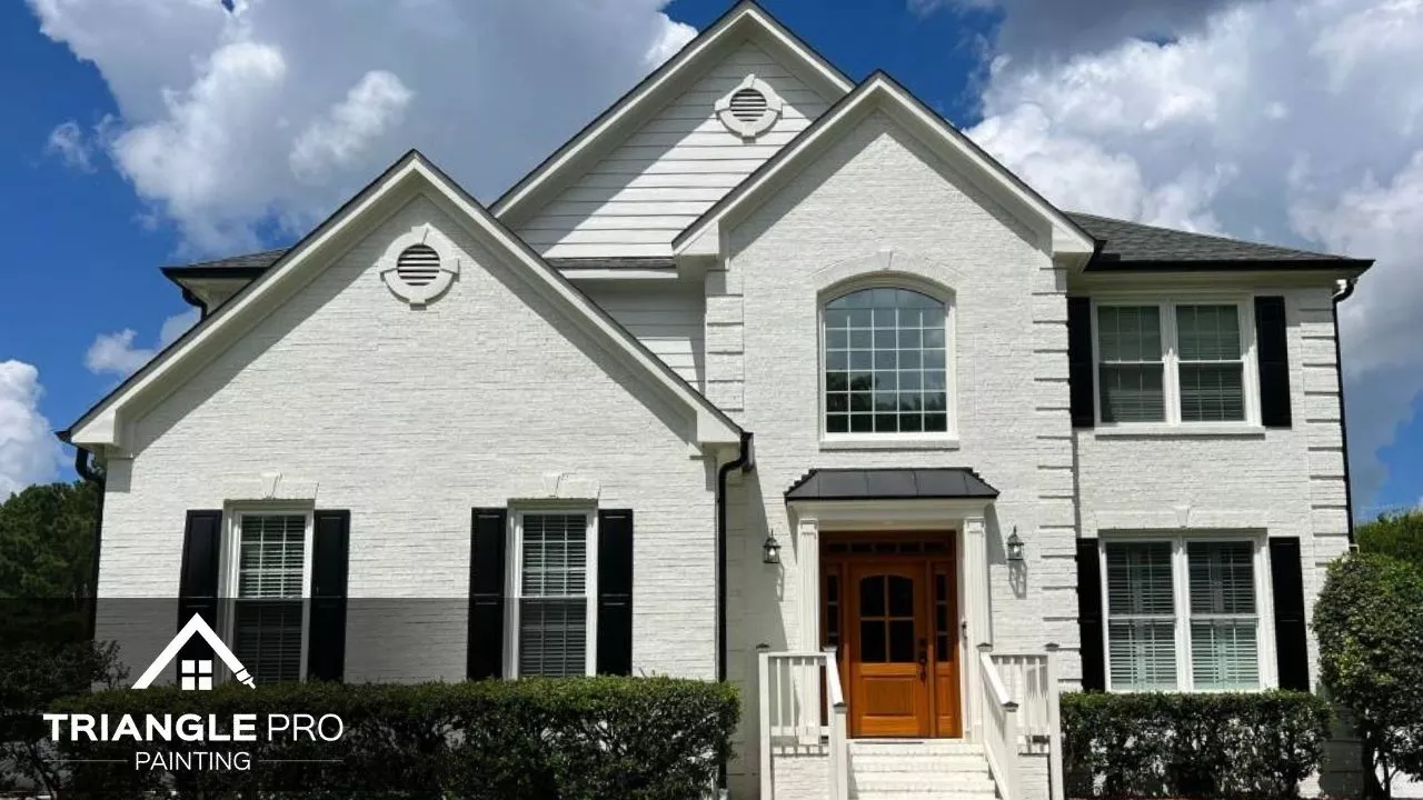 A beautifully finished white brick exterior with black shutters and a wooden door, painted by Triangle Pro Painting – offering a crisp, timeless curb appeal.